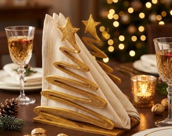 Può includere: Un portatovaglioli in metallo dorato a forma di albero di Natale stilizzato con una stella sulla punta, che contiene un tovagliolo di stoffa beige piegato. Il supporto presenta una finitura scintillante e poggia su una base rettangolare.
