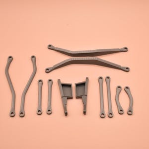 May include: A collection of gray plastic mechanical components including two long crossed bars, two curved side arms, four straight connecting rods, two small curved links, and two rectangular bracket pieces with protruding tabs.