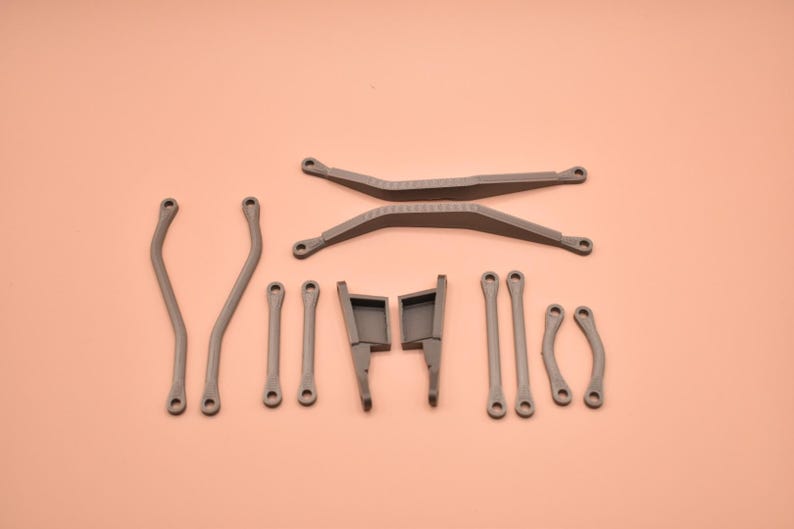 May include: A collection of gray plastic mechanical components including two long crossed bars, two curved side arms, four straight connecting rods, two small curved links, and two rectangular bracket pieces with protruding tabs.
