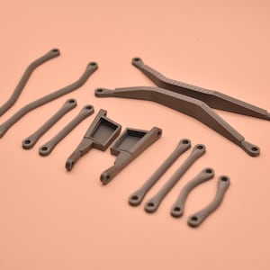 May include: A collection of dark gray, matte-finished plastic components for a remote-controlled vehicle, including two long curved suspension arms, two straight support bars, two angled chassis mounts, and four short curved links.