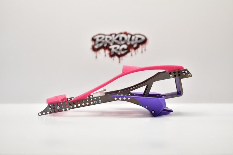 May include: A side profile of a radio-controlled car chassis featuring a dark metallic frame with numerous circular cutouts, a bright pink top rail, and a purple rear component. The logo BRKDUP RC is visible in the background.