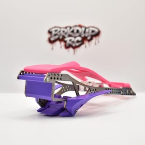 May include: A radio-controlled car chassis featuring a bright pink top section, a purple front bumper and lower components, and a dark grey metallic frame with perforated detailing. The logo BRKDP RC is visible in the background.