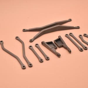 May include: A collection of dark gray, 3D-printed plastic mechanical components, including two long crossed bars, two curved rods, two straight rods, two angled brackets, and two small curved links, all featuring circular mounting holes.
