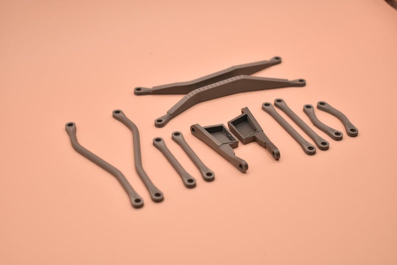 May include: A collection of dark gray, 3D-printed plastic mechanical components, including two long crossed bars, two curved rods, two straight rods, two angled brackets, and two small curved links, all featuring circular mounting holes.