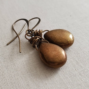 May include: A pair of gold-toned teardrop-shaped earrings with wire wrapped detailing. The earrings are suspended from simple silver hooks.