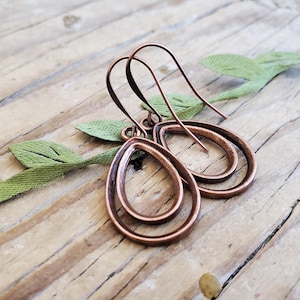 May include: A pair of copper teardrop earrings with a double-layered design. The earrings have a simple, minimalist style.