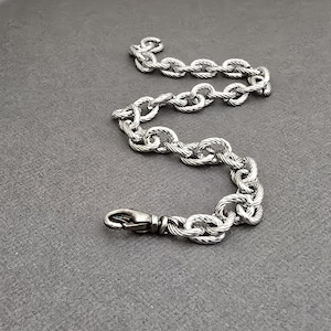 May include: A silver-toned chain bracelet featuring thick, twisted oval links with a textured, rope-like finish. The bracelet includes a secure lobster claw clasp at one end, designed to connect the links for a continuous, sturdy loop appearance.