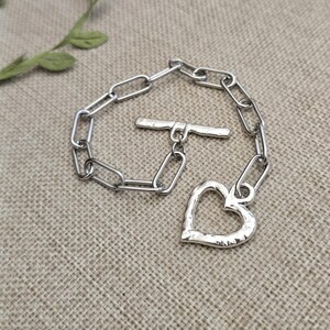 Pu&ograve; includere: Un braccialetto color argento con un ciondolo a forma di cuore e una chiusura a leva. Il braccialetto presenta un design a maglie di catena. Il ciondolo a forma di cuore ha una superficie strutturata.