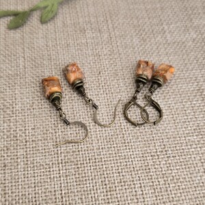 May include: Two pairs of handcrafted earrings. Each earring features a rectangular, speckled, orange and brown stone. The stones are attached to antique bronze-colored metal findings. One pair has a hook closure, and the other has a lever back closure.