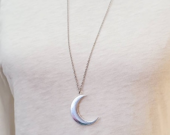 May include: A silver crescent moon pendant necklace on a silver chain. The necklace is displayed on a white mannequin.