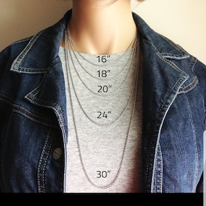 Pu&ograve; includere: Una persona indossa una maglietta grigia e una giacca di jeans, mostrando una collana a catena d'argento in varie lunghezze: 40 cm, 45 cm, 50 cm, 61 cm e 76 cm. La collana &egrave; esposta sul petto.