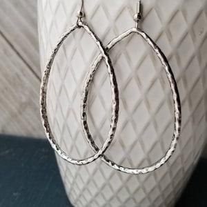 May include: A pair of silver oval hoop earrings with a hammered texture.