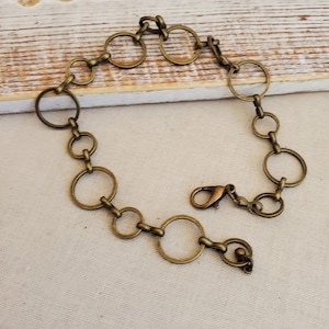 May include: An antique brass-toned bracelet featuring a series of interconnected circles. The bracelet has a lobster clasp closure. The design is simple and elegant, suitable for everyday wear or special occasions.