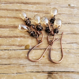 K&ouml;nnte beinhalten: Ein Paar Ohrringe aus Kupferdraht mit tropfenf&ouml;rmigen Glasperlen. Die Ohrringe sind handgefertigt und haben einen rustikalen, bohemian Stil.