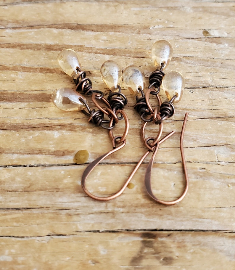 K&ouml;nnte beinhalten: Ein Paar Ohrringe aus Kupferdraht mit tropfenf&ouml;rmigen Glasperlen. Die Ohrringe sind handgefertigt und haben einen rustikalen, bohemian Stil.