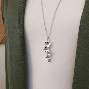 May include: A silver necklace with a pendant of five small, silver flowers. The flowers are arranged in a cascading pattern.