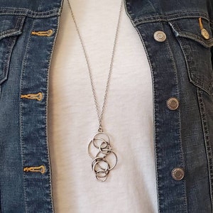 Puede incluir: Un collar de cadena de plata con un colgante hecho de varios círculos entrelazados.
