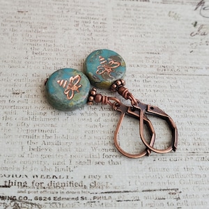 May include: A pair of copper hoop earrings with turquoise and gold bee charm pendants. The charms have a distressed, vintage look.
