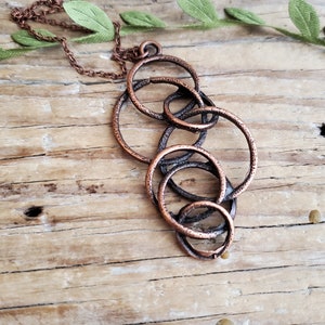 May include: A copper necklace with a pendant made of multiple interlocking circles. The circles are textured and have a rustic look.