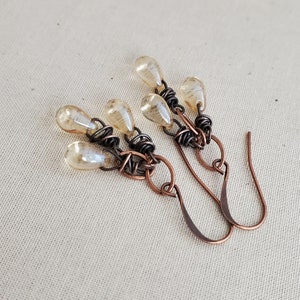 K&ouml;nnte beinhalten: Ein Paar Ohrringe mit einem Design aus Kupferdraht und mehreren tropfenf&ouml;rmigen Glasperlen in einer hellbernsteinfarbenen Farbe.