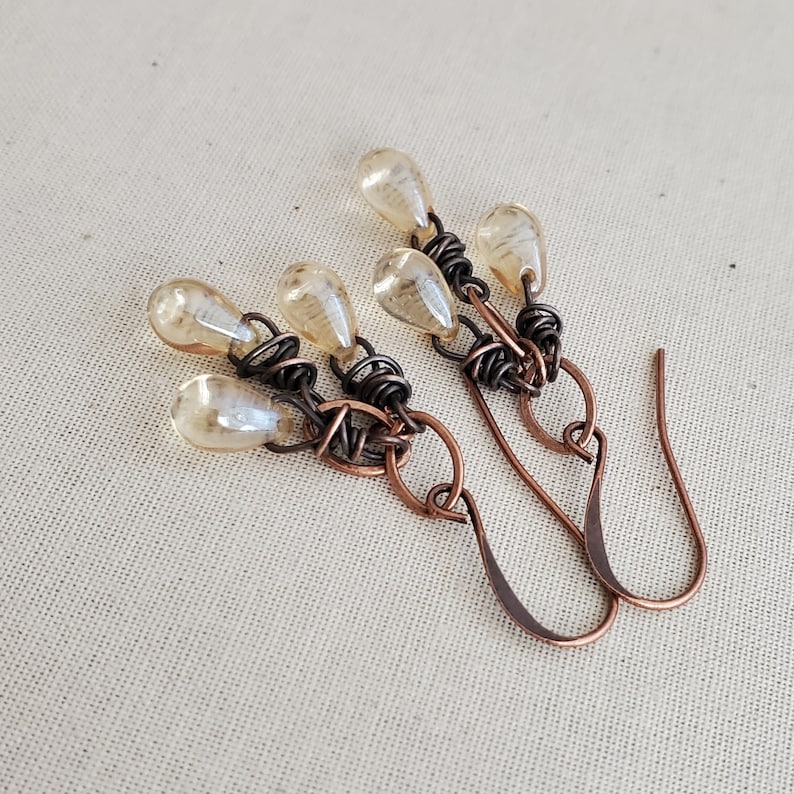 K&ouml;nnte beinhalten: Ein Paar Ohrringe mit einem Design aus Kupferdraht und mehreren tropfenf&ouml;rmigen Glasperlen in einer hellbernsteinfarbenen Farbe.