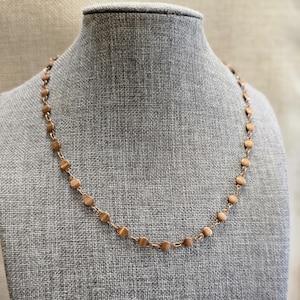 Può includere: Una collana color oro rosa caratterizzata da una catena delicata intervallata da piccoli dischi metallici circolari e piatti. La collana presenta un design uniforme con elementi rotondi equidistanti collegati da sottili maglie metalliche.