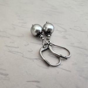 May include: A pair of silver-colored earrings featuring large, round, pearl-like beads. The beads are attached to lever-back closures. The earrings have a vintage or antique aesthetic, with a simple yet elegant design. The earrings are likely made of metal.