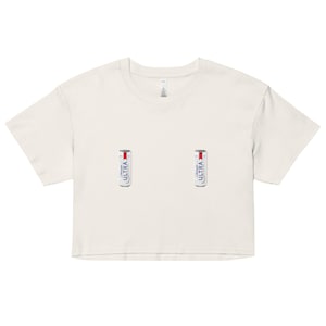 May include: Cream-colored crop top with two beer can graphics. The cans are white with red and blue accents and the word "ULTRA" printed vertically. The shirt has short sleeves and a crew neck.