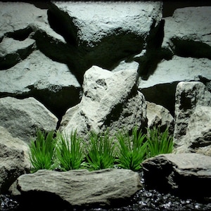 May include: A decorative aquarium background featuring a rock formation with green plants. The background is made of gray rocks and has a dark, shadowy appearance. The plants are a vibrant green color.