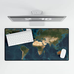 May include: A rectangular desk mat featuring a detailed world map design in shades of blue, green, and brown. A white keyboard and mouse are positioned on the mat. A computer monitor is visible above the mat.