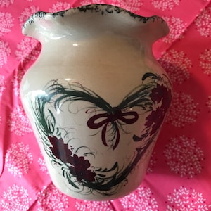 May include: A white ceramic vase with a scalloped rim and a hand-painted design of a green wreath with a red bow and burgundy flowers.