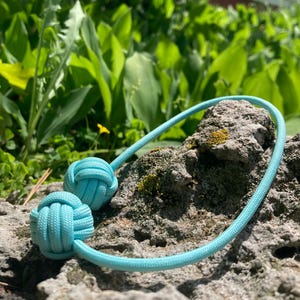 May include: A pair of light blue rope knots tied together with a long loop of the same rope.