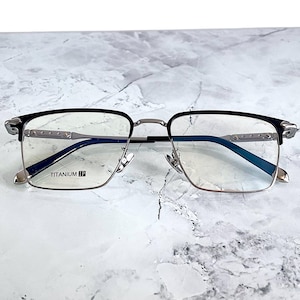 Titanium rectangular eyeglass frames in black and silver with golden temple accents. Suitable for prescription or fashion lenses. Includes hard ETE case, soft pouch, and cleaning cloth. Lightweight, durable, and hypoallergenic design for men and women. Ideal as a stylish gift with fast worldwide shipping.