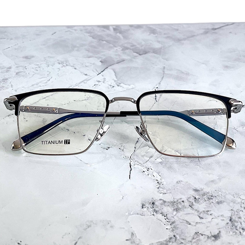 Titanium rectangular eyeglass frames in black and silver with golden temple accents. Suitable for prescription or fashion lenses. Includes hard ETE case, soft pouch, and cleaning cloth. Lightweight, durable, and hypoallergenic design for men and women. Ideal as a stylish gift with fast worldwide shipping.