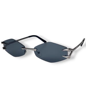 Puede incluir: Gafas de sol sin montura con lentes grises oscuros en forma de diamante y detalles plateados. Las patillas son negras y la montura tiene un diseño único en forma de garra en las esquinas de las lentes.