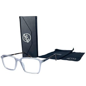 Könnte beinhalten: Brille mit transparentem Rahmen, schwarzem Etui und zwei schwarzen Reinigungstüchern. Die Brille hat eine rechteckige Form und einen transparenten Rahmen. Das Etui ist schwarz mit weißem Logo. Die Tücher sind schwarz mit weißem Logo.