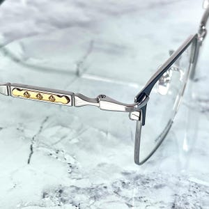 Titanium rectangular eyeglass frames in black and silver with golden temple accents. Suitable for prescription or fashion lenses. Includes hard ETE case, soft pouch, and cleaning cloth. Lightweight, durable, and hypoallergenic design for men and women. Ideal as a stylish gift with fast worldwide shipping.