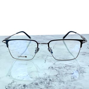 Titanium rectangular eyeglass frames in black and silver with golden temple accents. Suitable for prescription or fashion lenses. Includes hard ETE case, soft pouch, and cleaning cloth. Lightweight, durable, and hypoallergenic design for men and women. Ideal as a stylish gift with fast worldwide shipping.
