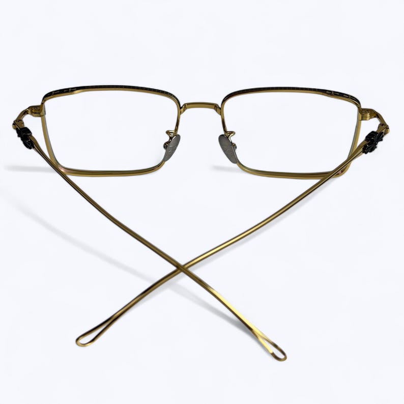 May include: Gold-toned rectangular eyeglasses with clear lenses. The frames have a delicate design, with a thin bridge and temples that cross at the back. The temples have decorative accents near the hinges.
