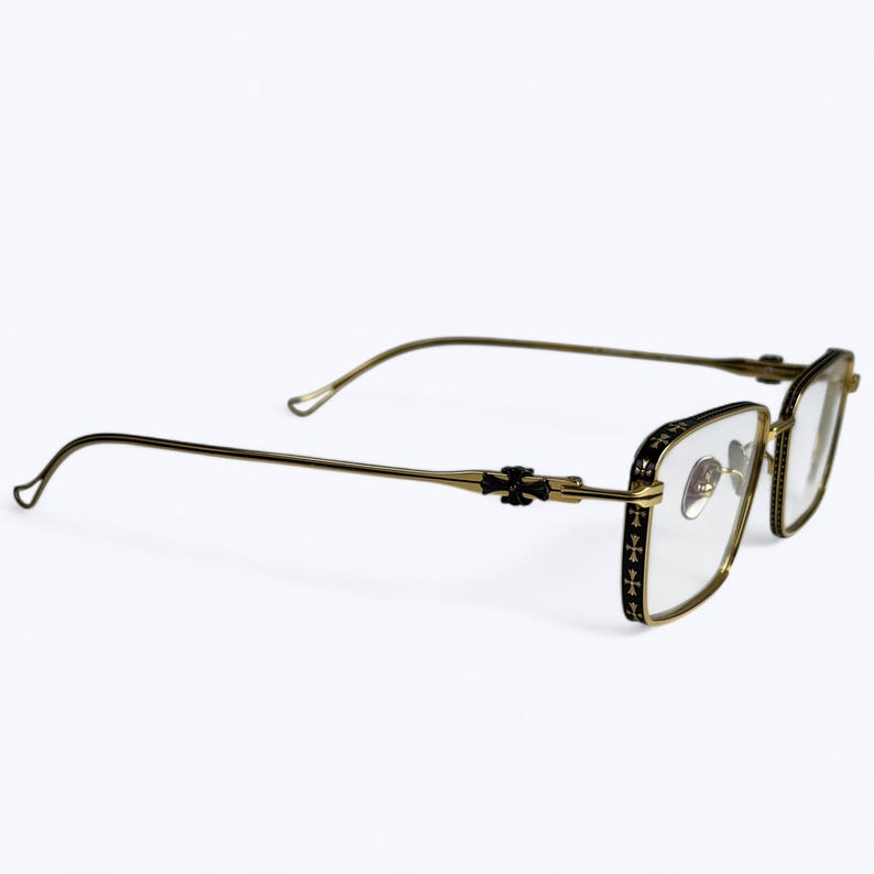 May include: Gold-toned eyeglasses with a rectangular frame and clear lenses. The frame features black detailing with a cross pattern on the temples and hinges. The arms curve gently for a comfortable fit.