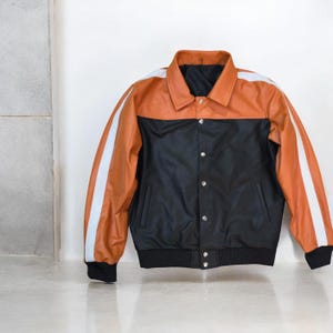 May include: A two-tone jacket with a black body and a tan upper section. White stripes run down the sleeves. The jacket has a collared neckline and a button-up front. The cuffs and hem are black.