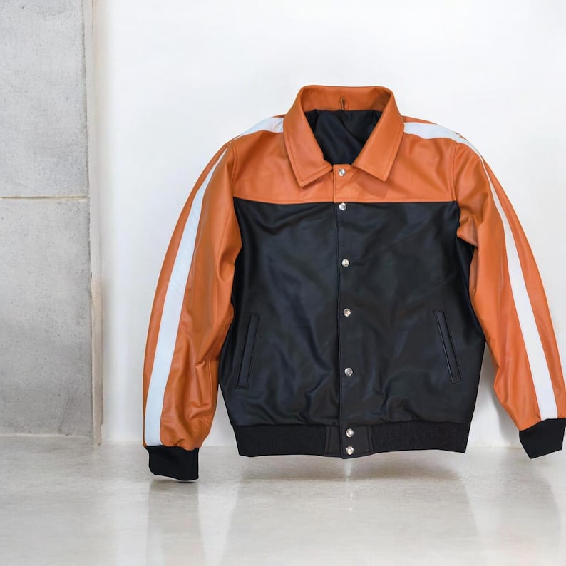 May include: A two-tone jacket with a black body and a tan upper section. White stripes run down the sleeves. The jacket has a collared neckline and a button-up front. The cuffs and hem are black.