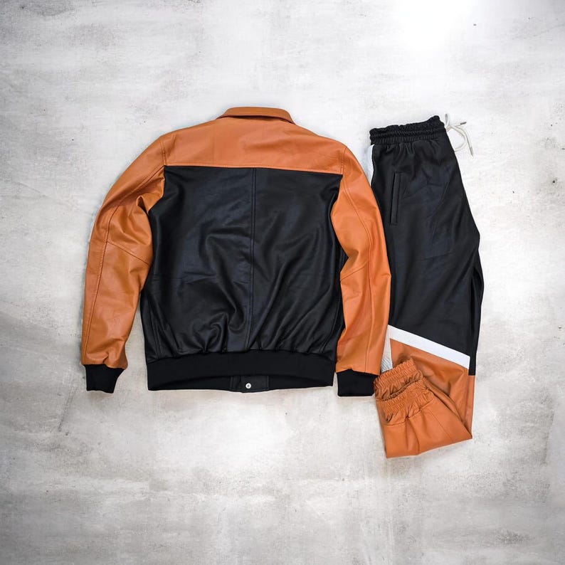 May include: A two-tone leather jacket and matching track pants set. The jacket is black with tan sleeves and a tan collar. The track pants are black with a white and tan stripe down the side. The set is displayed on a gray surface.