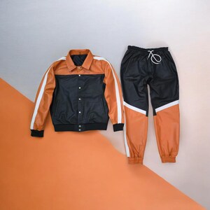 May include: A two-piece athletic set featuring a black and orange jacket and matching pants. The jacket has a collared neckline, white stripes on the sleeves, and a black bottom. The pants are black with orange panels and a white stripe.