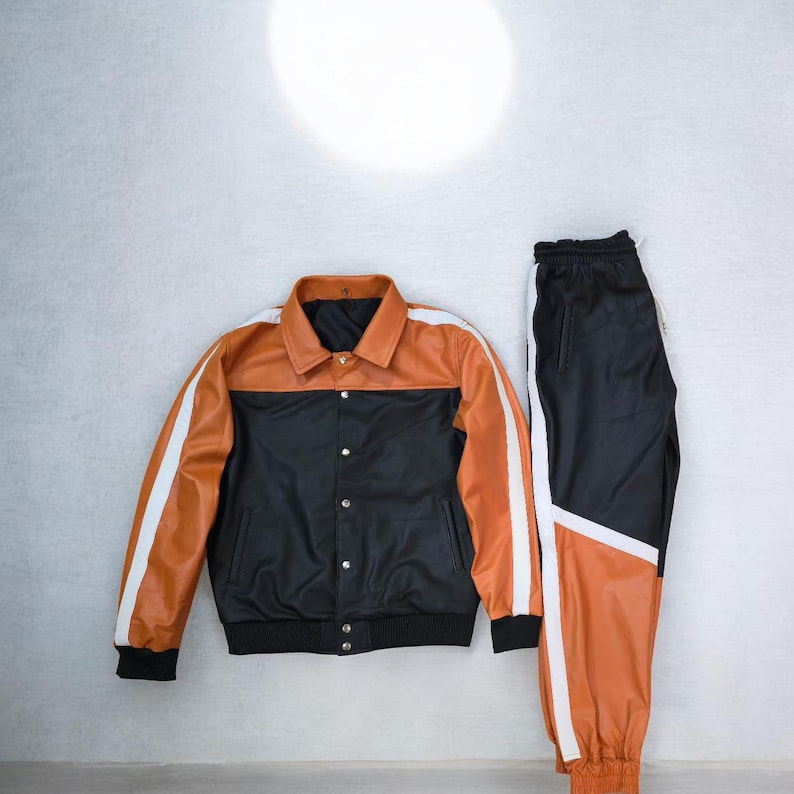 May include: A two-piece athletic set featuring a black and orange jacket and matching pants. The jacket has a black body with an orange yoke and white stripes on the sleeves. The pants are black with orange panels and white stripes.