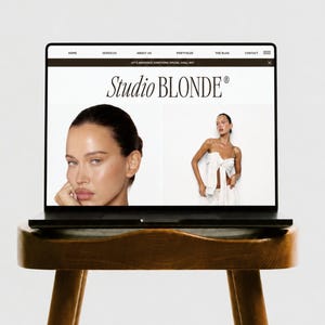 May include: A black laptop displaying a website with the text Studio BLONDE, featuring a navigation bar with Home, Services, About Us, Portfolio, The Blog, and Contact, and two photographs of a person with dark hair in a white top.