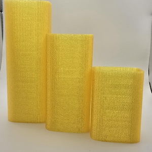 May include: Three yellow, rectangular, textured decorative pillars of varying heights. The pillars have rounded corners and a consistent color, creating a cohesive set. The tallest pillar is approximately 10 inches tall.