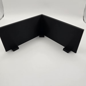 May include: A black, right-angled display stand. The stand is made of a solid material and has two supporting feet. The stand is designed to hold items at a 90-degree angle, perfect for displaying items.
