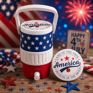 May include: A cylindrical beverage cooler with a white handle and a spigot, featuring a blue section with white stars and a red base. The lid and a separate circular coaster display the text America, Land of the Free, Because of the Brave.