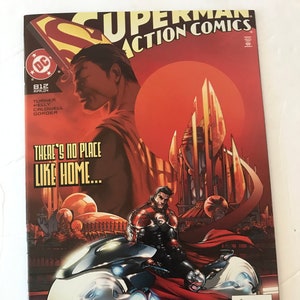 May include: Superman Action Comics #812 comic book cover featuring Superman riding a futuristic motorcycle in front of a red sun and a cityscape. The cover text reads "There's no place like home..."